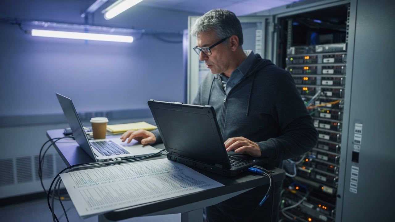 Administrator at a desk comparing a classic forum tree on one monitor with a modern topic list on another, a printed cutover checklist between them