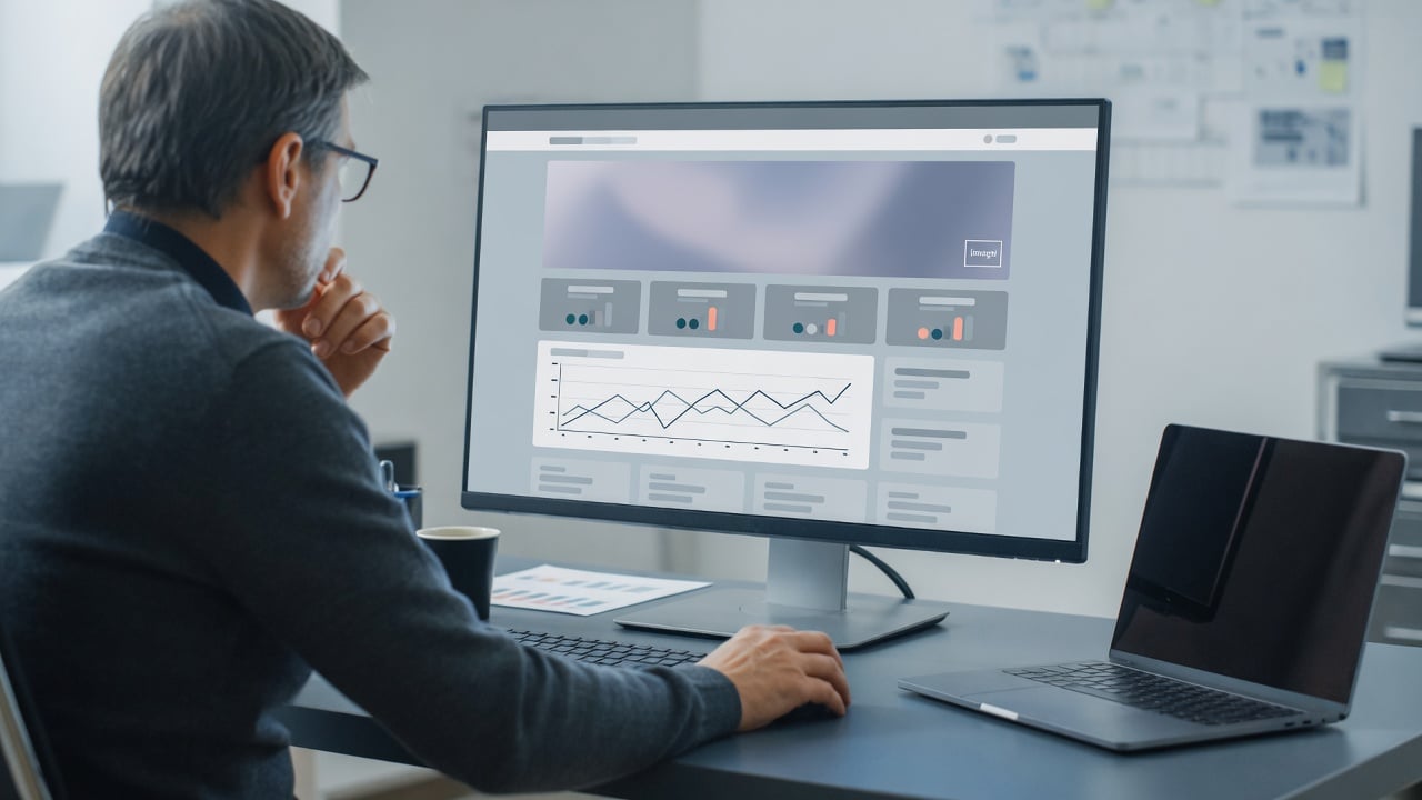 Administrator reviewing forum performance charts on a widescreen monitor in a cool steel-blue office